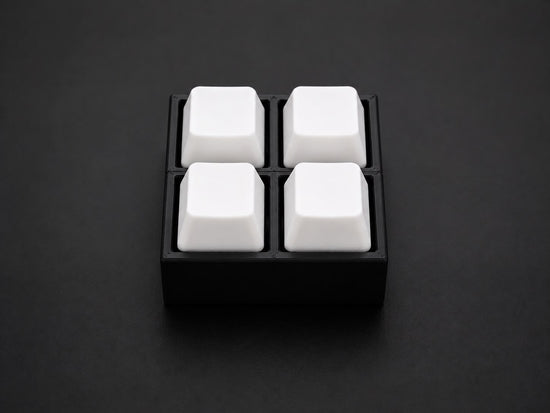 Clack Fidget Clicker 4-Key Square, a 3D-printed matte black desk toy with four white mechanical keycaps, front view